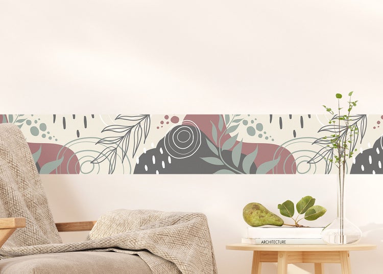Wandbordüre mit abstraktem Berg- und Blattmuster in einem hellen, modern eingerichteten Wohnzimmer über einem Sofa.