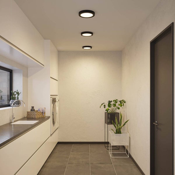 Moderner Hauswirtschaftsraum mit drei runden schwarzen Deckenleuchten, hellen Schränken, grauem Fliesenboden und Zimmerpflanzen.