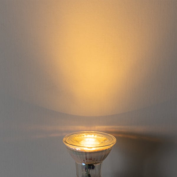 Eingeschaltete LED-Reflektorlampe mit warmweißem Lichtkegel an einer Wand.