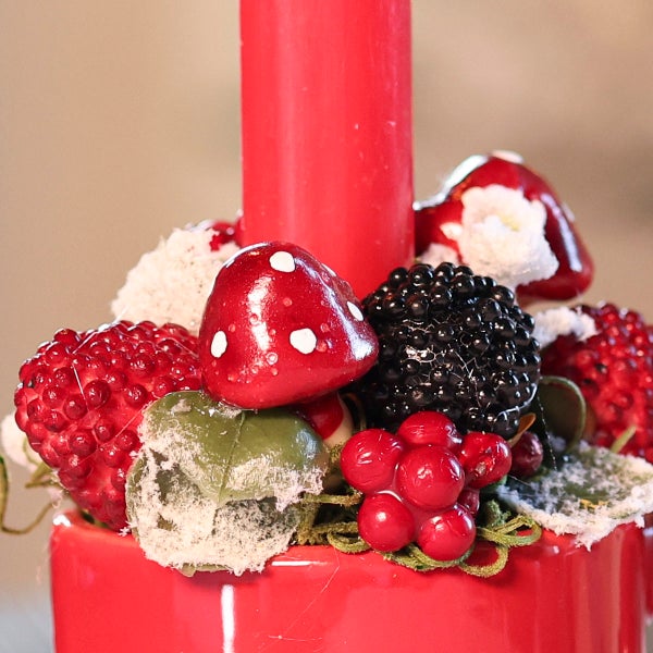 Weihnachtsdekoration mit Stabkerze und künstlichen Beeren sowie Fliegenpilzen als Tischschmuck.