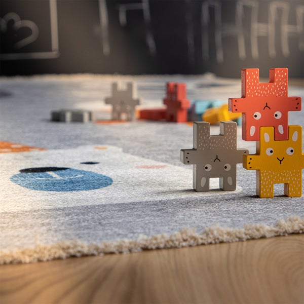 Kinderspielteppich mit Bärenmotiv und bunte Holzspielzeugfiguren in Hasenform auf einem Holzboden