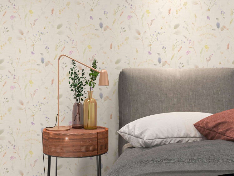 Vliestapete mit zartem Wiesenblumenmuster in einem Schlafzimmer, kombiniert mit einem Nachttisch, einer Tischleuchte und einem Bett.
