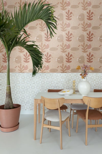 Esszimmer mit Esstisch, Stühlen und dekorativer Palme im Topf vor einer gemusterten Tapete.