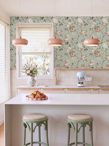 Helle Küche mit floraler Tapete mit Rosenmuster, rosa Pendelleuchten und einer weißen Kücheninsel mit grünen Barhockern.