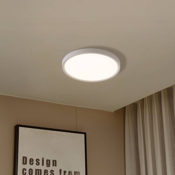 Flache runde LED Deckenleuchte montiert an einer hellen Decke in einem modern eingerichteten Wohnraum mit Vorhang und Bild.