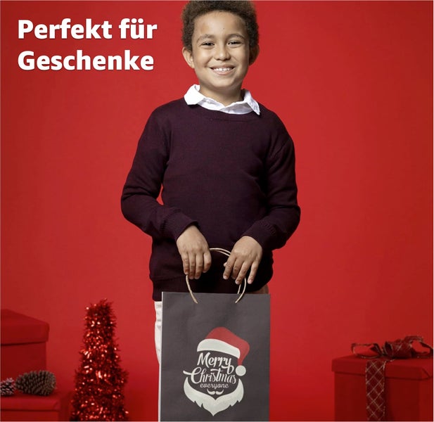 Junge hält Geschenktüte mit Weihnachtsmotiv vor rotem Hintergrund