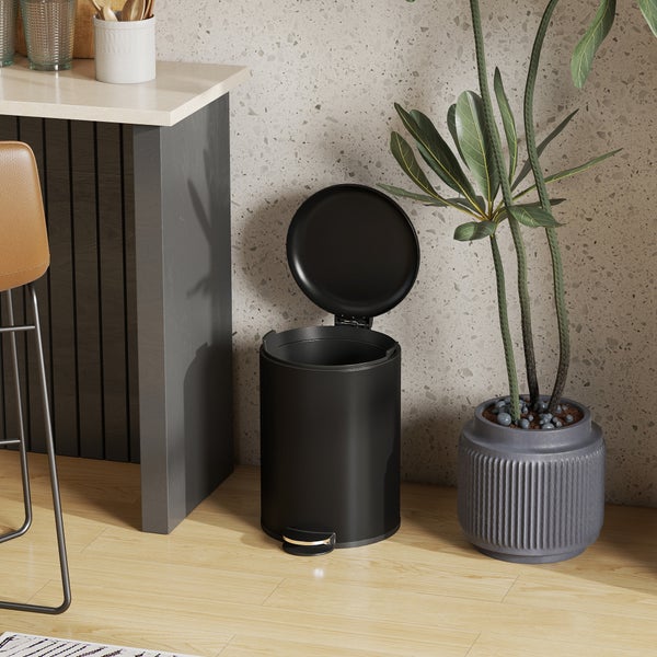Schwarzer Tretabfalleimer mit offenem Deckel in einer modernen, hellen Küche neben einer Zimmerpflanze auf Holzboden.