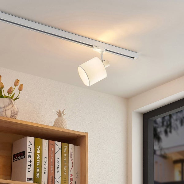 Modernes Schienensystem mit einem zylindrischen Spot an einer weißen Decke über einem Holzregal in einem hellen Raum.