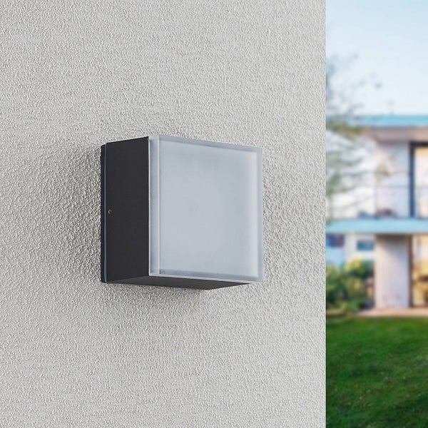 Quadratische Außenwandleuchte mit dunklem Metallgehäuse und mattierter Abdeckung an einer hellen Hauswand.