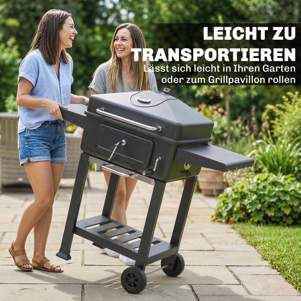 Zwei Frauen rollen einen schwarzen Holzkohlegrill auf Rädern über eine gepflasterte Terrasse im Garten.