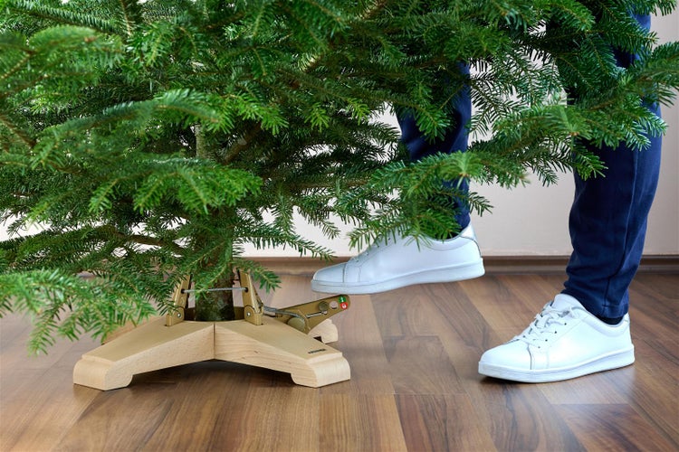 Person fixiert einen Weihnachtsbaum in einem hölzernen Christbaumständer