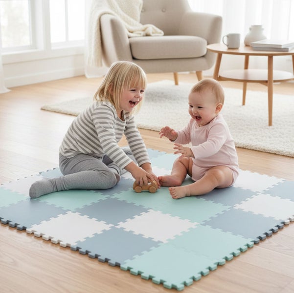 Zwei Kinder spielen fröhlich auf einer quadratischen Spielmatte aus ineinandergreifenden Schaumstoffelementen in einem hellen Wohnzimmer.