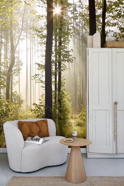 Einrichtungsidee mit Waldtapete, Sessel, Holztisch und weißem Schrank für ein helles und organisiertes Ambiente.