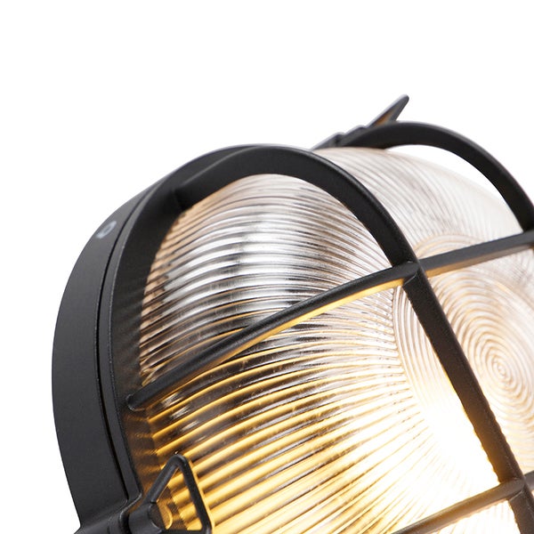 Nahaufnahme einer schwarzen Außenwandleuchte mit Metallkäfig und geriffeltem Glas, die warmes Licht ausstrahlt.