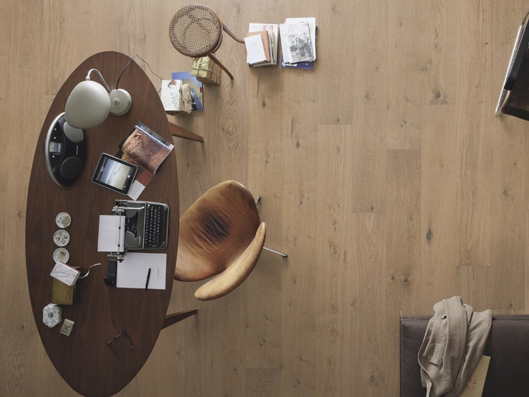 Draufsicht auf einen hellen Parkettboden in einem Arbeitszimmer mit ovalem Schreibtisch, Schreibmaschine und Lederstuhl.
