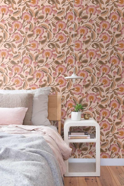 Helles Schlafzimmer mit floral gemusterter Tapete, hellem Bett, Holzkopfteil und einem weißen Beistelltisch.