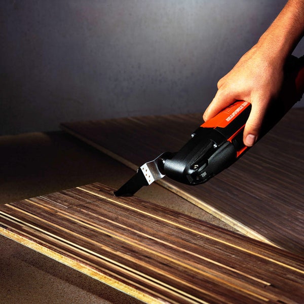 Eine Hand bedient ein Multifunktionswerkzeug zum Schneiden eines Holzbretts.