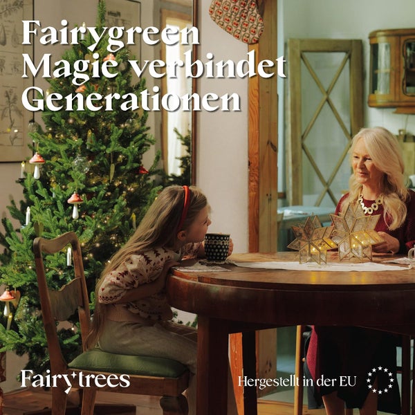 Eine Frau und ein Kind sitzen gemütlich an einem Holztisch neben einem geschmückten Weihnachtsbaum mit FairyTrees Beleuchtung in einem Wohnraum.