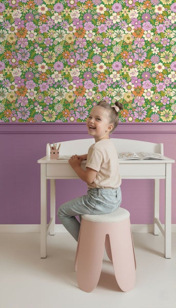 Mädchen sitzt an einem Schreibtisch vor einer grünen Tapete mit Blumenmuster.