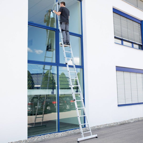Mann reinigt Fenster mit einer Mehrzweckleiter an einem Gebäude.