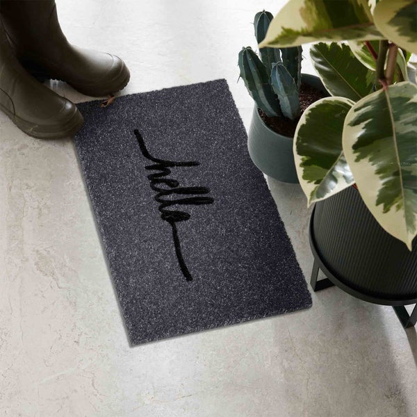 Fußmatte mit dem Schriftzug Hallo, Gummistiefel und Topfpflanzen auf dem Boden