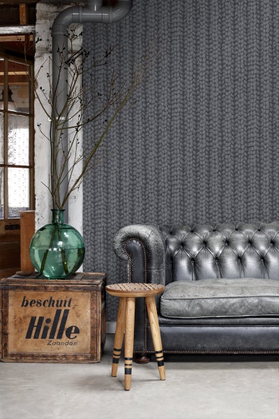 Wohnraum mit Strickmuster-Tapete, Ledersofa und Holzhocker