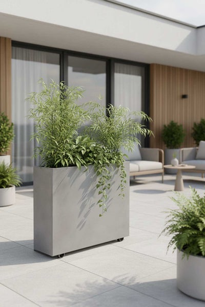 Großer, grauer Pflanzkübel auf Rollen mit hohen Gräsern auf einer modernen, hellen Terrasse mit Lounge-Möbeln.