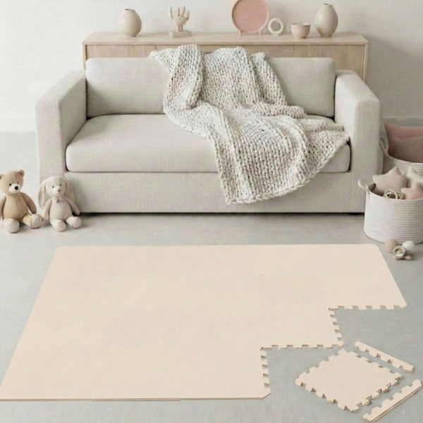 Puzzle-Spielmatte aus Schaumstoff im hellen Wohnzimmer vor einem Sofa mit Kuscheltieren. Matte aus ineinandergreifenden Teilen.