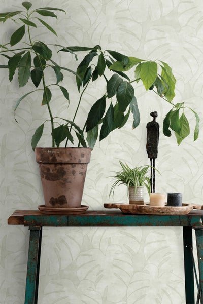 Dekoratives Interieur mit Pflanze in Terrakotta-Topf auf einem Tisch vor einer gemusterten Tapete.
