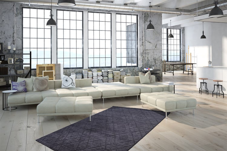 Großes, helles Loft mit industriellem Stil, bodentiefen Fenstern, beigem Wohnlandschaft-Sofa, Holzboden und dunklem Teppich im Wohnbereich.
