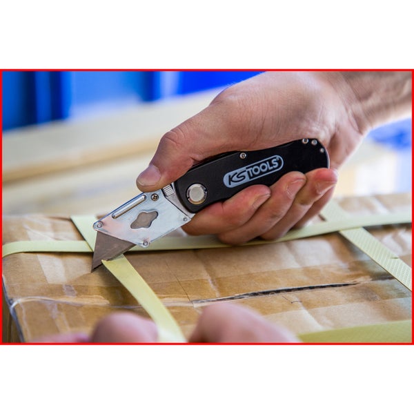 Eine Hand schneidet mit einem KS Tools Klappmesser ein Umreifungsband auf einem Versandkarton auf.