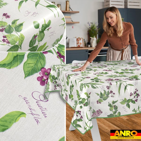 Helle, organisierte Küche mit einer Frau, die eine Wachstuch-Tischdecke mit botanischem Muster aus grünen Blättern und lila Blüten auflegt.