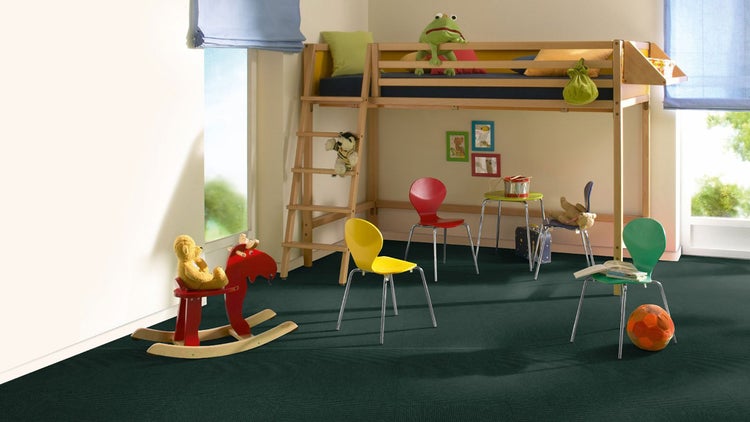 Dunkelgrüne Teppichfliesen in einem hellen Kinderzimmer mit einem hölzernen Hochbett, bunten Stühlen und verschiedenen Spielzeugen.