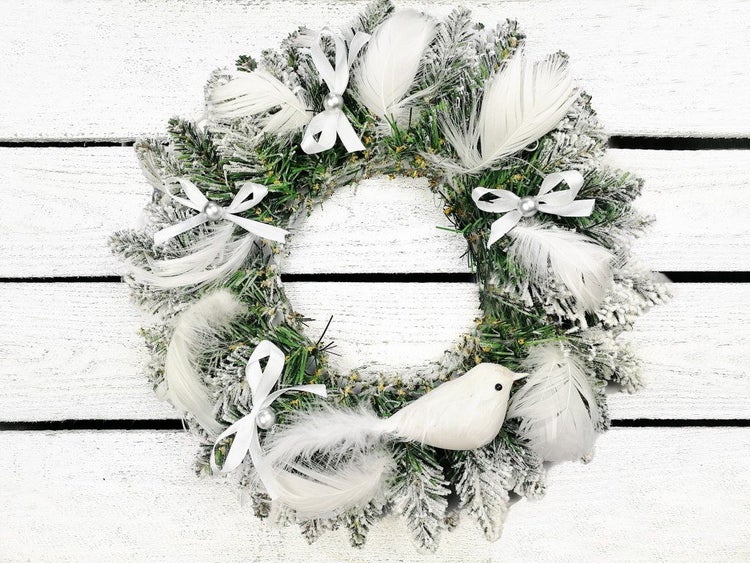 Weihnachtskranz aus künstlichen Tannenzweigen mit Kunstschnee, Federn, Schleifen und einer Vogelfigur zur festlichen Dekoration.