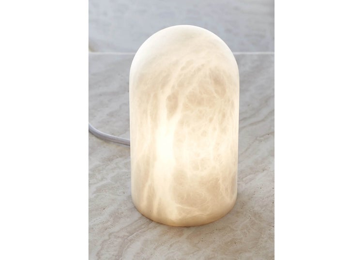 Tischleuchte aus Alabaster in Kuppelform mit weichem Lichtschein auf einer passenden Steinplatte stehend.