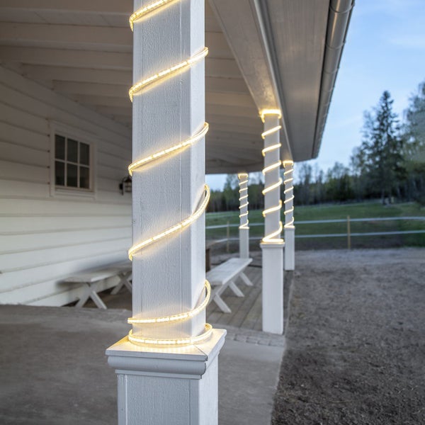 Beleuchtete LED-Lichterschläuche umwickeln weiße Säulen auf einer Veranda.