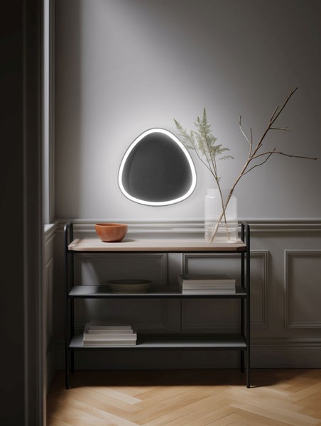 Organisch geformte Wandleuchte mit LED-Beleuchtung über einem schwarzen Metallregal in einem modern eingerichteten Raum.