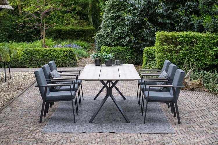 Moderne Garten-Essgruppe mit rechteckigem Gartentisch in Holzoptik und sechs gepolsterten Gartenstühlen auf einem Outdoorteppich im Garten.