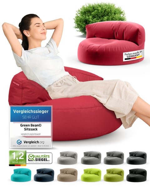 Eine Frau entspannt sich auf einem roten Green Bean Sitzsack, der mit dem Vergleichssieger-Siegel und dem Qualitätssiegel ausgezeichnet ist. Ein weiterer Sitzsack und ein grüner Busch sind im Hintergrund zu sehen.