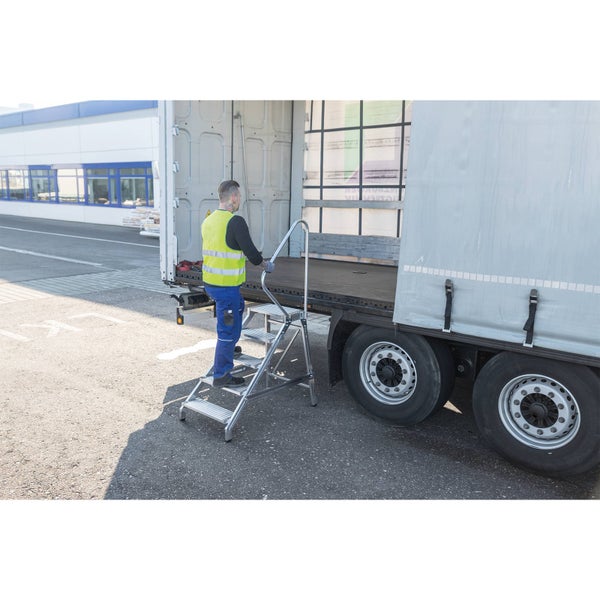 Eine Person steigt über eine mobile Arbeitsplattform mit Handlauf in einen LKW Auflieger.