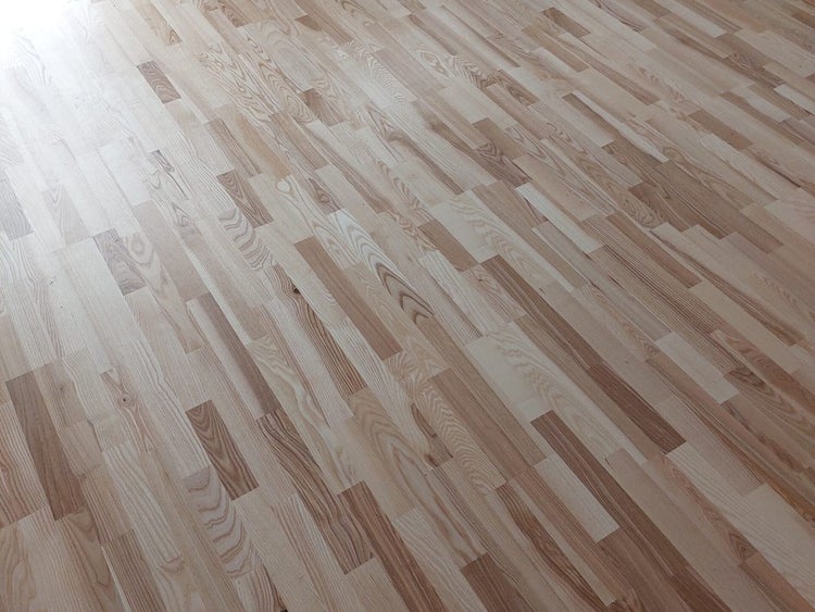 Parkettboden aus hellem Holz mit Schiffsboden-Muster und ausgeprägter Maserung.