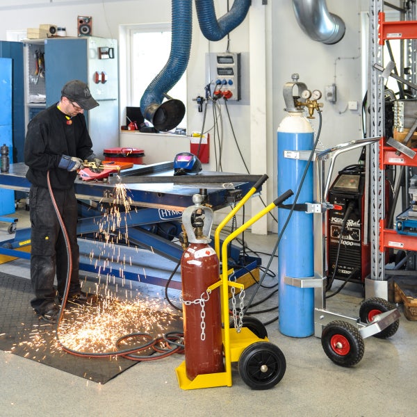 Ein Mann bei der Metallbearbeitung mit einem Schweißbrenner in einer Werkstatt, zusammen mit Zubehör wie Gasflaschenwagen und Schweißgeräten.
