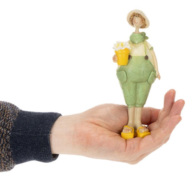 Dekorationsfigur Mädchen mit Hut, grünem Overall und gelbem Blumentopf, in einer Hand gehalten zur Darstellung der Größe.