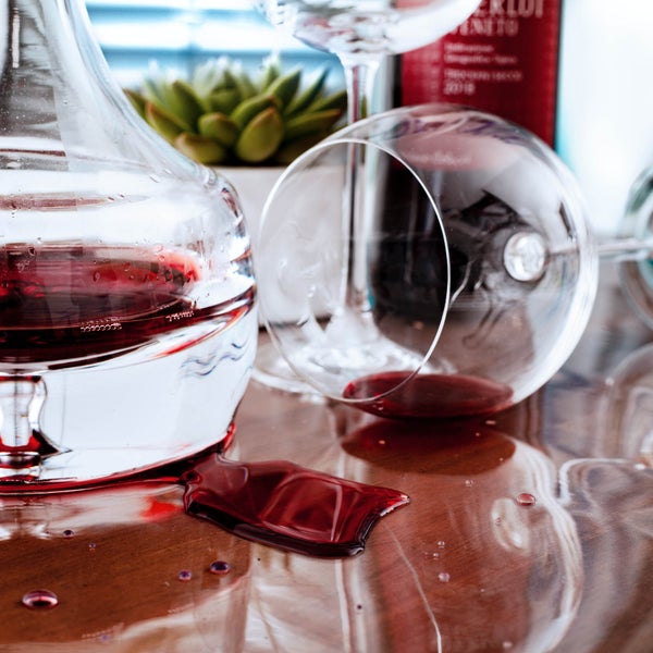 Verschütteter Rotwein auf einer Holzoberfläche neben einer Glaskaraffe und einem umgekippten Weinglas.