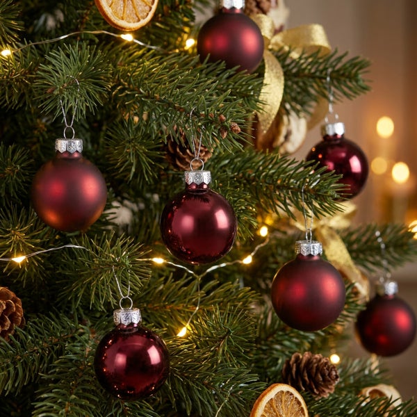 Weihnachtsbaum mit mattem und glänzendem Christbaumschmuck, Kiefernzapfen und Lichterkette als festliche Dekoration.