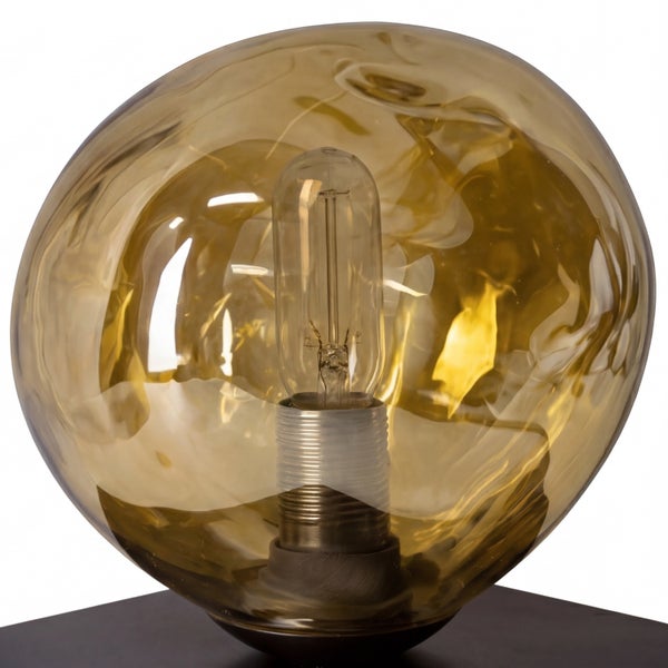 Dekorative Tischleuchte mit wellenförmigem bernsteinfarbenem Glasschirm und sichtbarer länglicher Glühbirne auf einem dunklen Sockel.