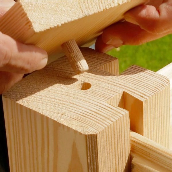 Hände montieren ein Holzelement mittels eines Holzdübels in einen massiven Holzpfosten.