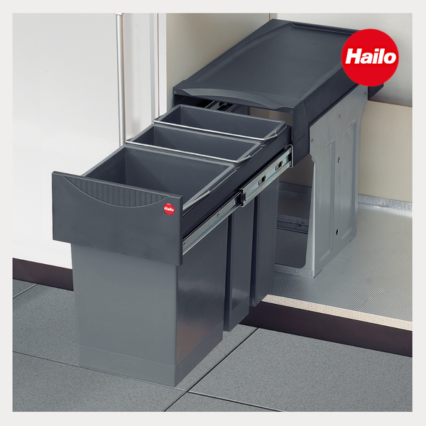 Einbau-Abfallsammler von Hailo mit Metallauszug und grauer Frontblende, der von einer Hand geöffnet wird. Hailo Logo.