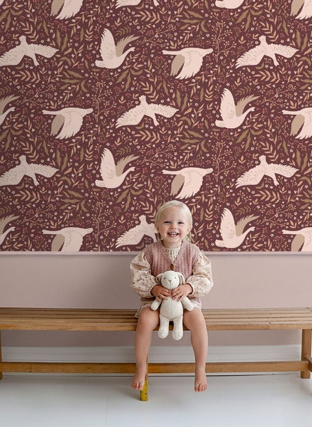 Mädchen sitzt vor einer Wand mit Vogelmuster-Tapete auf einer Holzbank