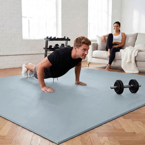 Ein Mann macht Liegestütze auf einer großen grauen Fitnessmatte in einem hellen Wohnzimmer mit Parkettboden.